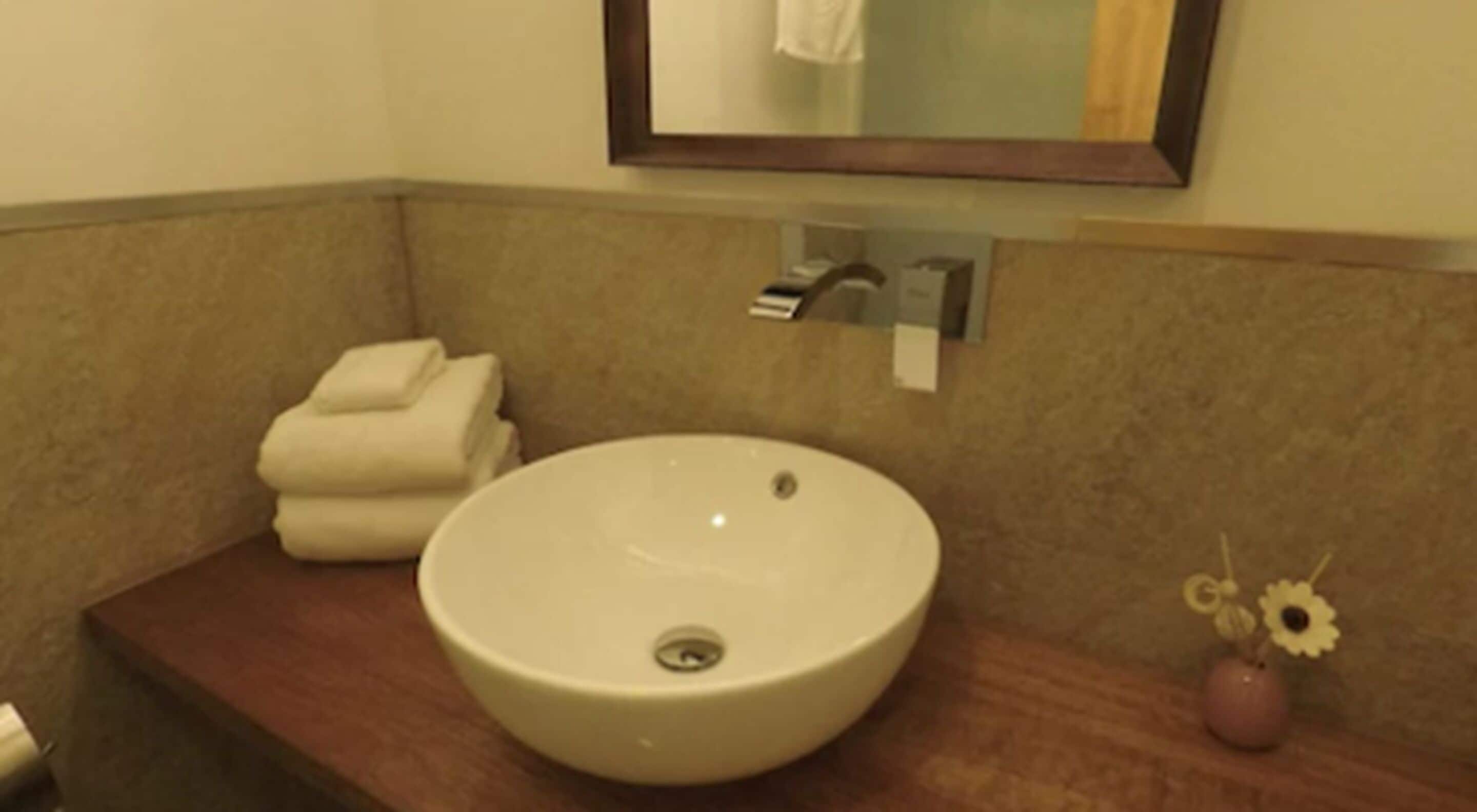 A bathroom with a round sink, a towel stack, and a mirror above the sink.