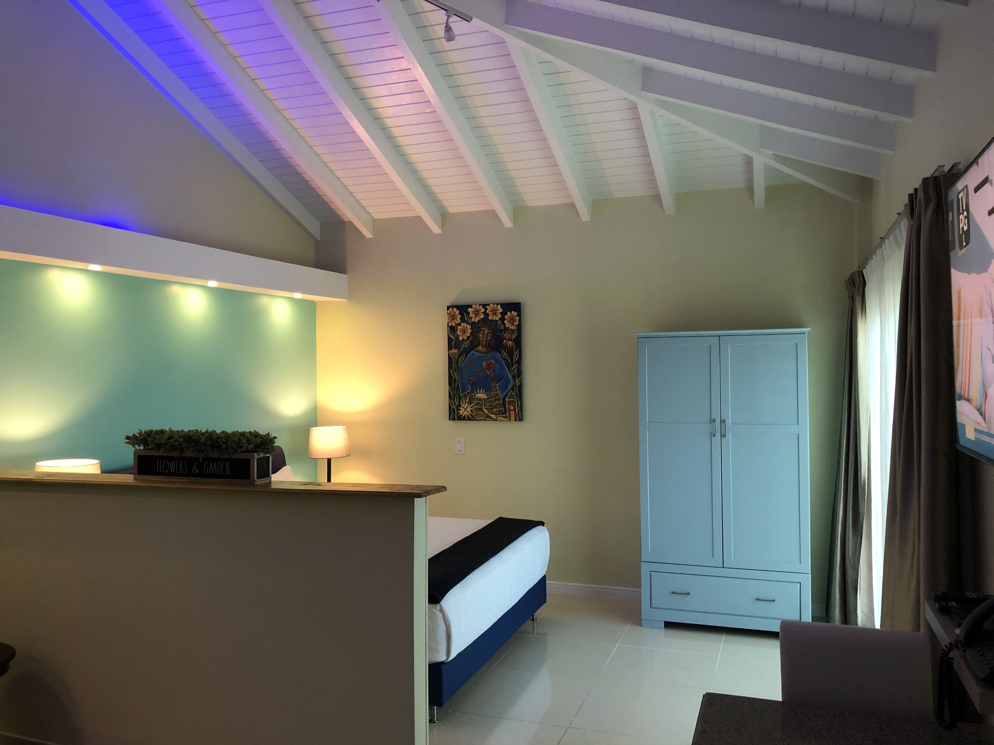 Een slaapkamer met een bed, een kledingkast, een bureau met een lamp en een schilderij aan de muur.