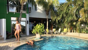 Una piscina con sillas de descanso, palmeras y un edificio de fachada verde.