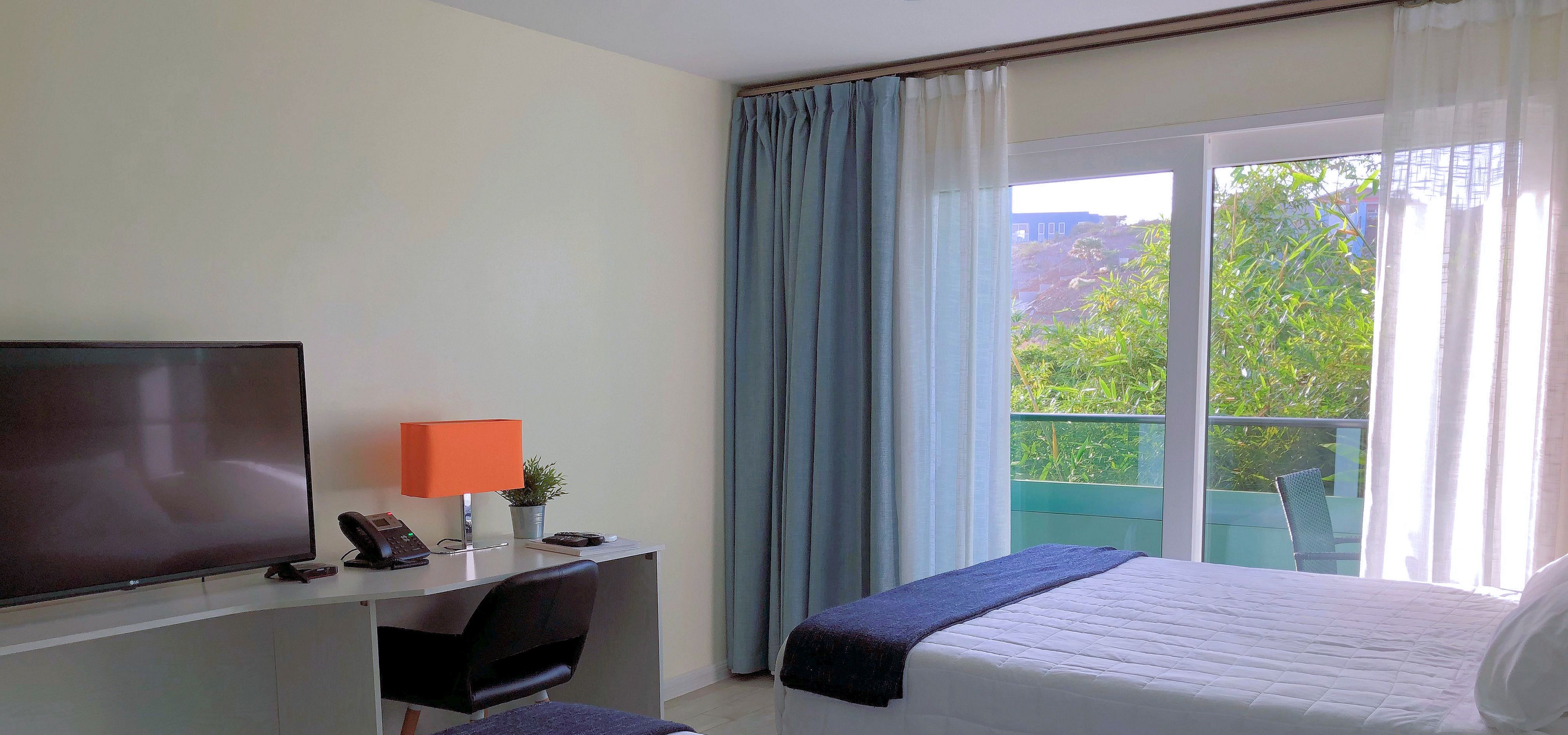 A hotel room with two beds, a desk with a TV, phone, and lamp, and a window with curtains.