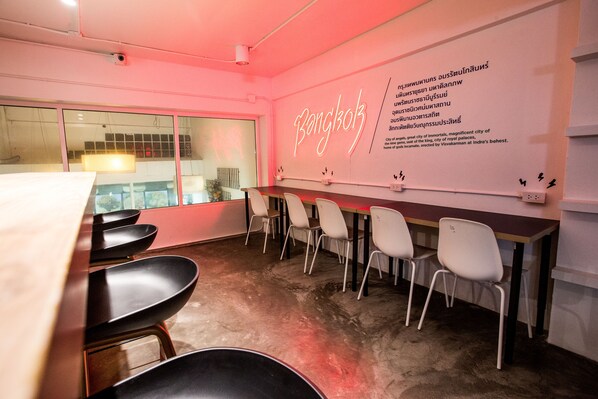 A modern office space with a long table and several chairs, a neon sign reading "Bangkok", and a wall with text describing the city. - HQ hostel Silom (Bangkok)