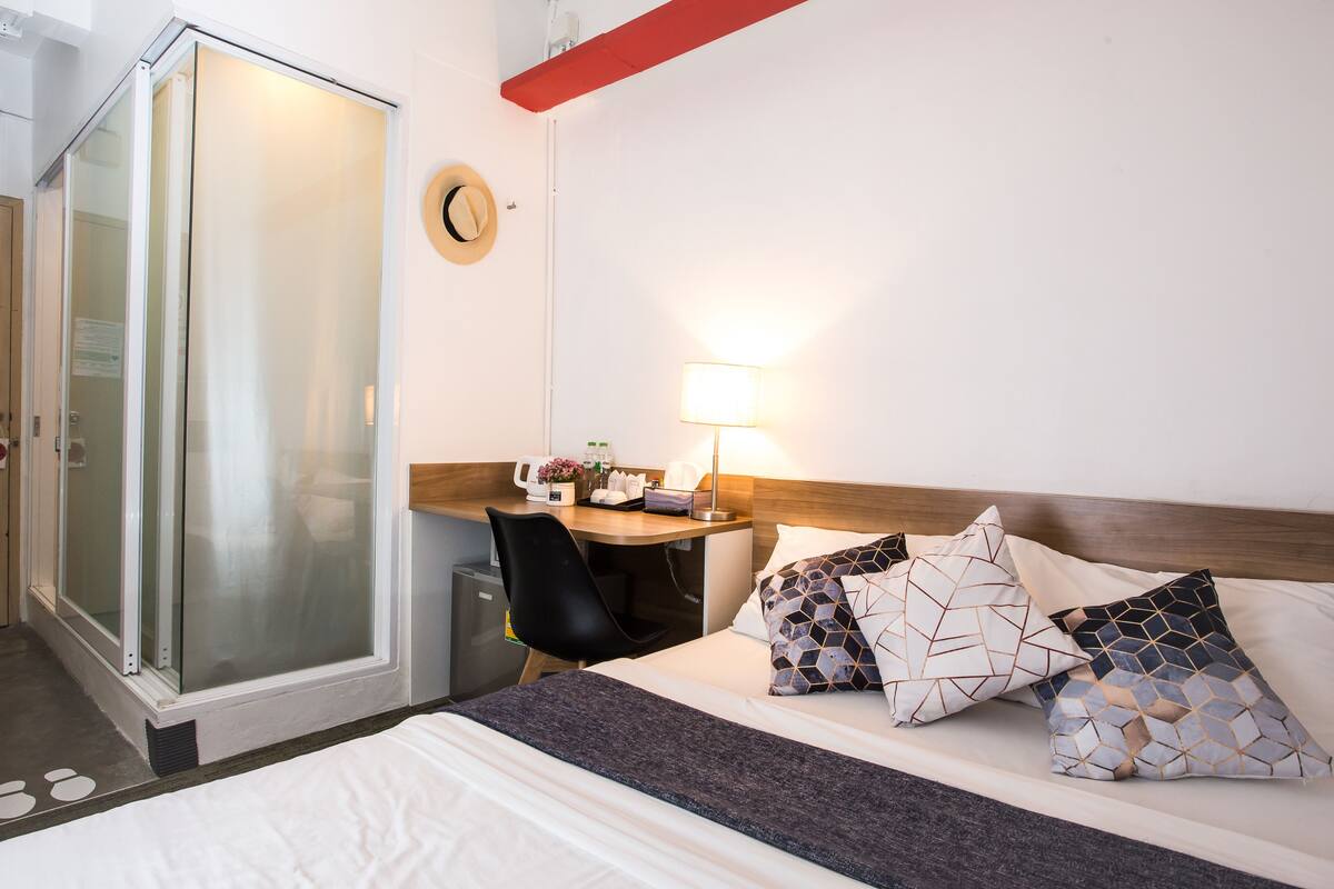 A hotel room with a bed, a desk, a chair, a shower, and a wall clock.