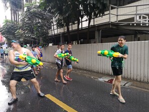 A group of people walking down a wet street, some holding water guns. - HQ hostel Silom (Bangkok)
