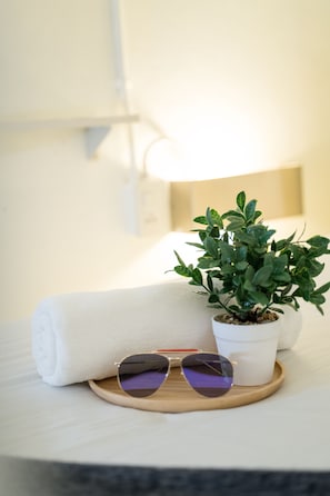 A neatly made bed with a rolled white towel, a small potted plant, and a pair of sunglasses on a wooden tray.