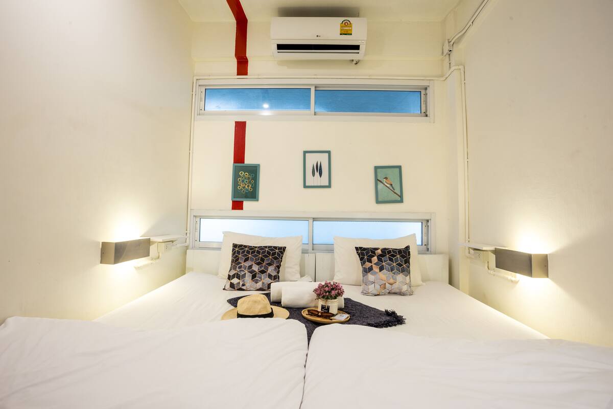 A hotel room with a bed, two wall-mounted lamps, a window, and a wall-mounted air conditioner.
