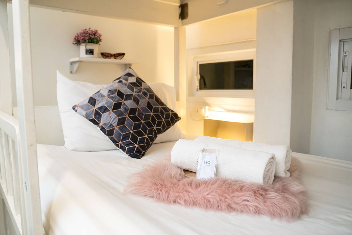 A neatly made bed with a rolled white towel, a black and white patterned pillow, and a pink fluffy pillow.