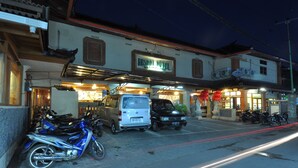 A hotel with a signboard, parked vehicles, and a paved street. - Rosani Hotel (Legian)