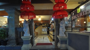 A hotel entrance with a red carpet, stone statues, and a security sign. - Rosani Hotel (Legian)