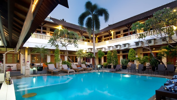 A hotel pool area with multiple lounge chairs, a pool, and potted plants. - Rosani Hotel (Legian)
