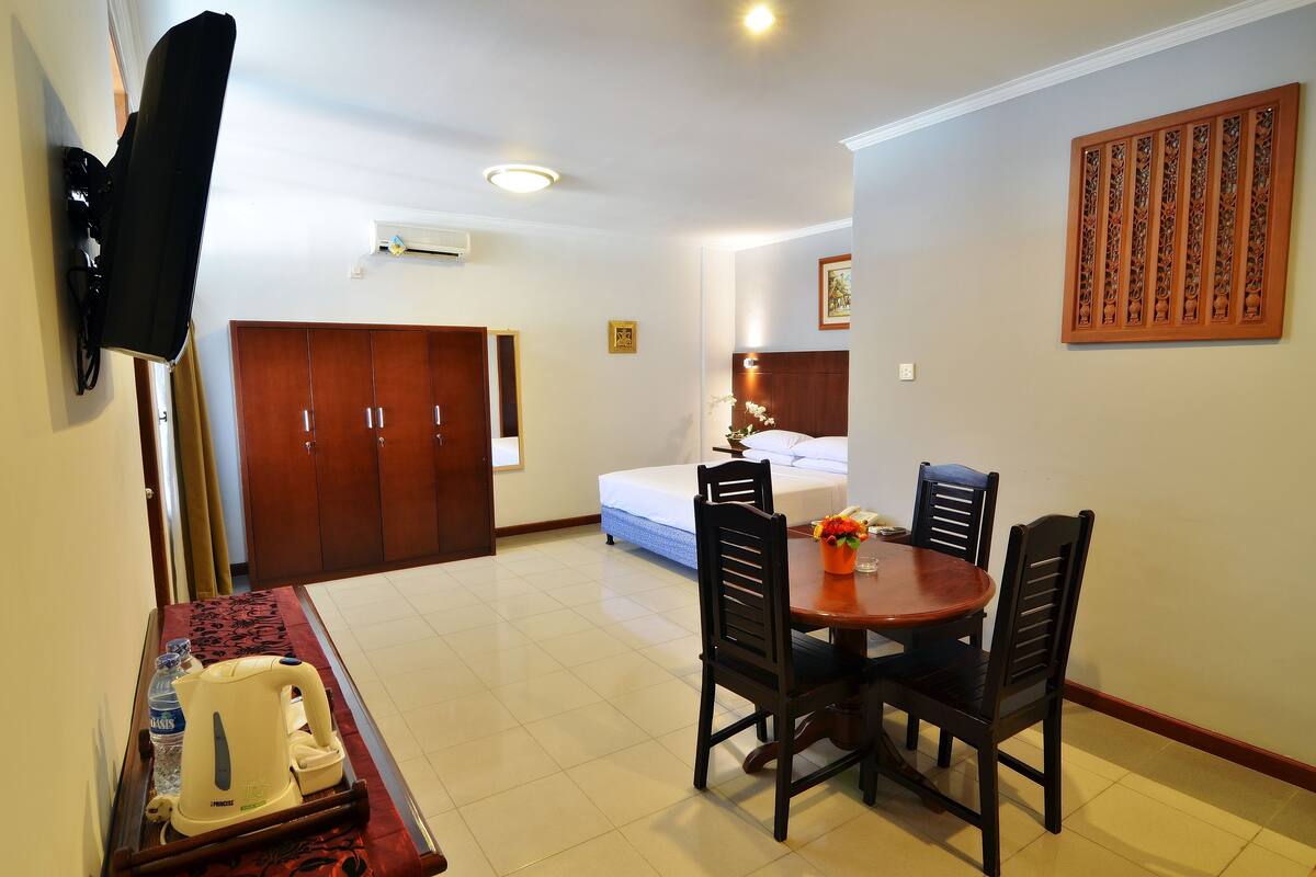 A hotel room with a dining area, a bed, a TV mounted on the wall, and a wooden cabinet.