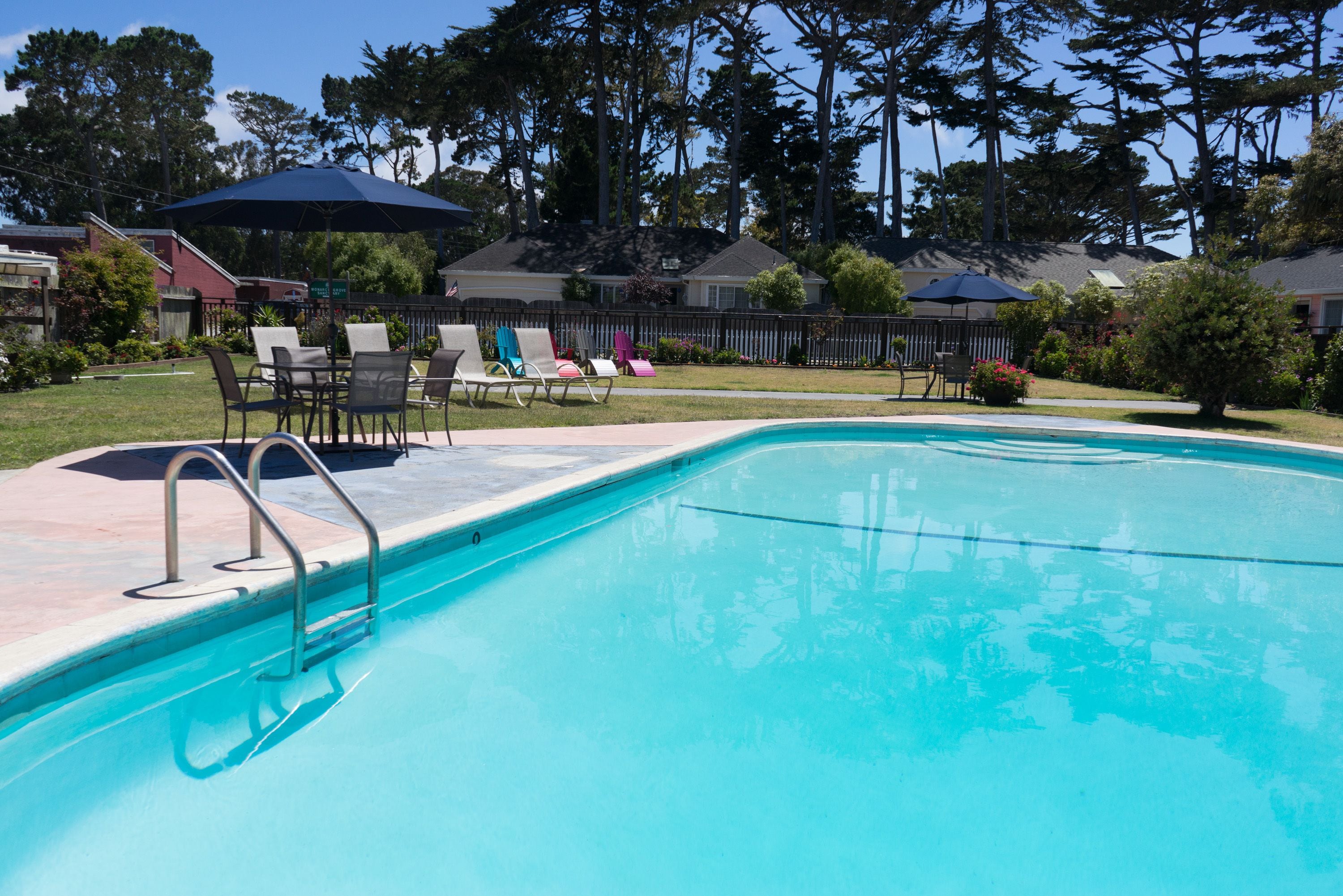 A swimming pool with a metal ladder, surrounded by lounge chairs and umbrellas.