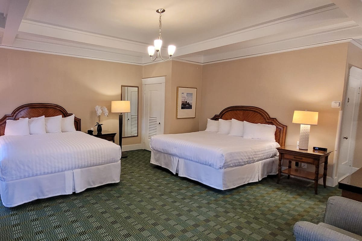 A hotel room with two beds, a chandelier, a desk, and a chair.