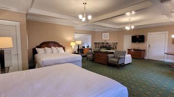 Quarto de hotel com duas camas, área de refeições, televisão e lustre.