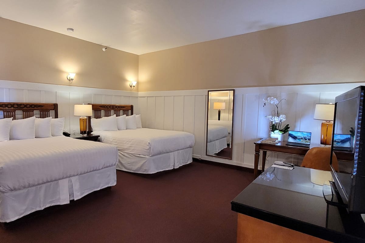 A hotel room with two beds, a desk with a computer, a mirror, and a lamp.