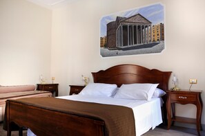 Une chambre d’hôtel avec un grand lit, deux tables de chevet, une petite table et un tableau représentant un bâtiment, accroché au mur.