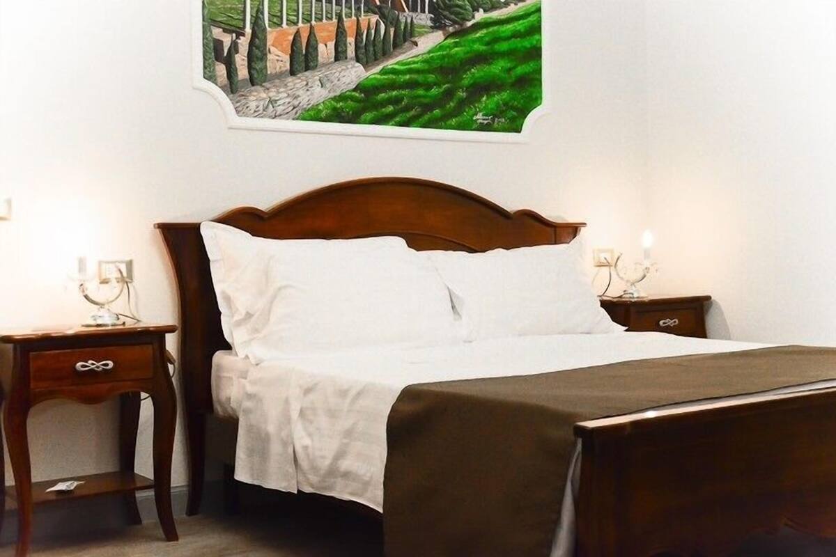 A neatly made bed with white linens, a wooden headboard, and a nightstand with a lamp.