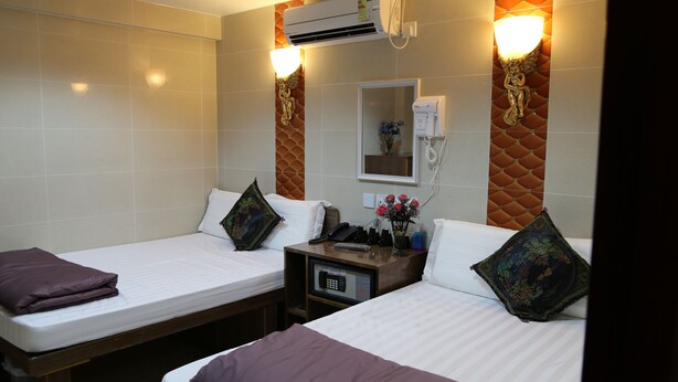 A hotel room with two beds, a bedside table with a phone and a remote control, and an air conditioning unit mounted on the wall. - Tokyo Hostel (Kowloon)
