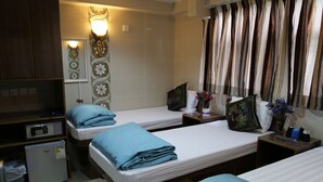 A hotel room with two single beds, a small refrigerator, a bedside table with a lamp, and a wall-mounted light fixture. - Tokyo Hostel (Kowloon)