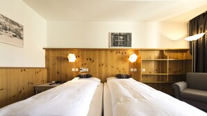 Quarto de hotel com duas camas de solteiro, cabeceira de madeira, prateleiras fixadas na parede, uma mesa e uma cadeira.