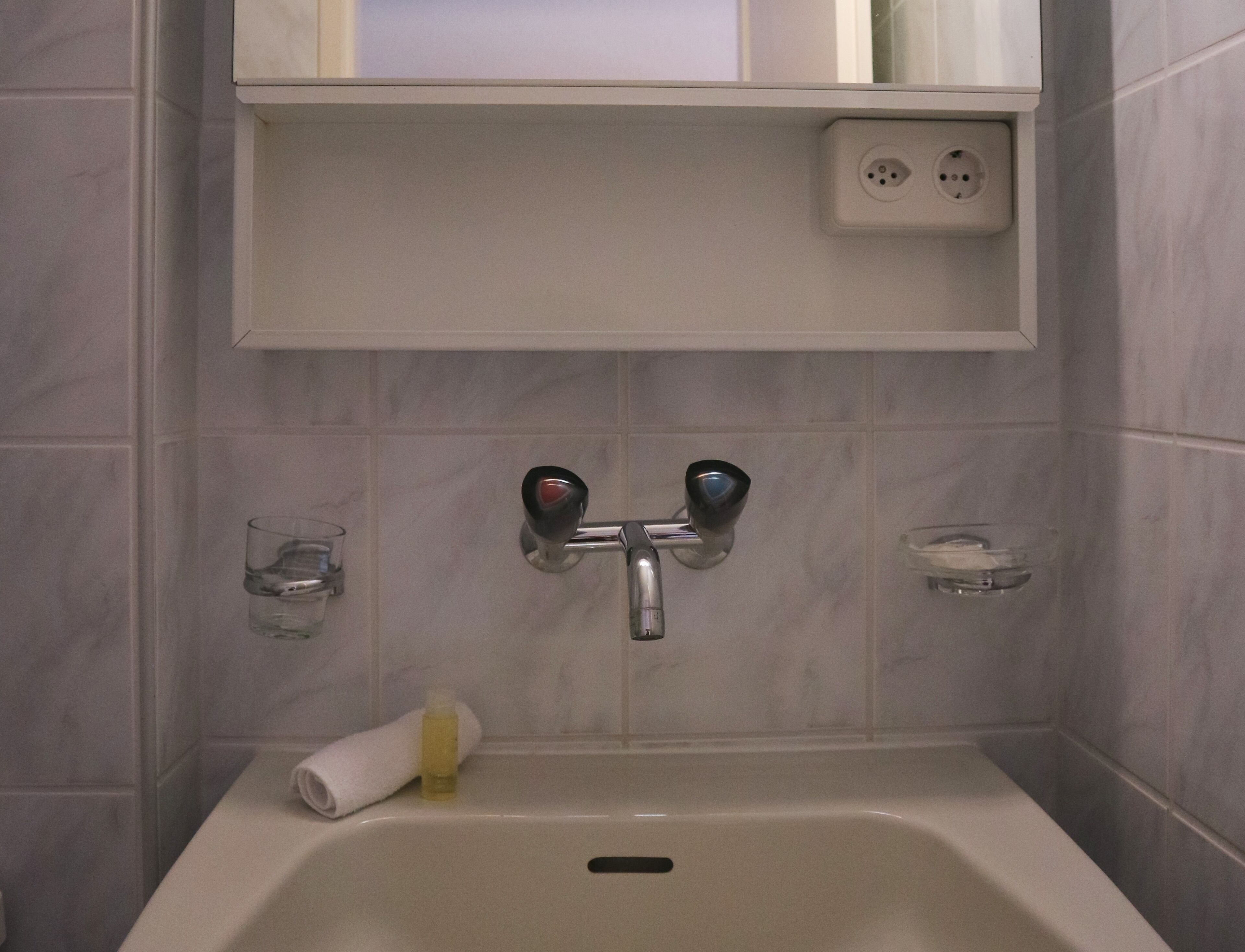 Un baño con una bañera blanca, una toalla, un jabonero de vidrio y un enchufe en la pared.