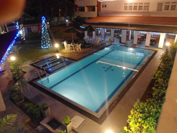 A swimming pool with a tiled deck, surrounded by potted plants and outdoor furniture.