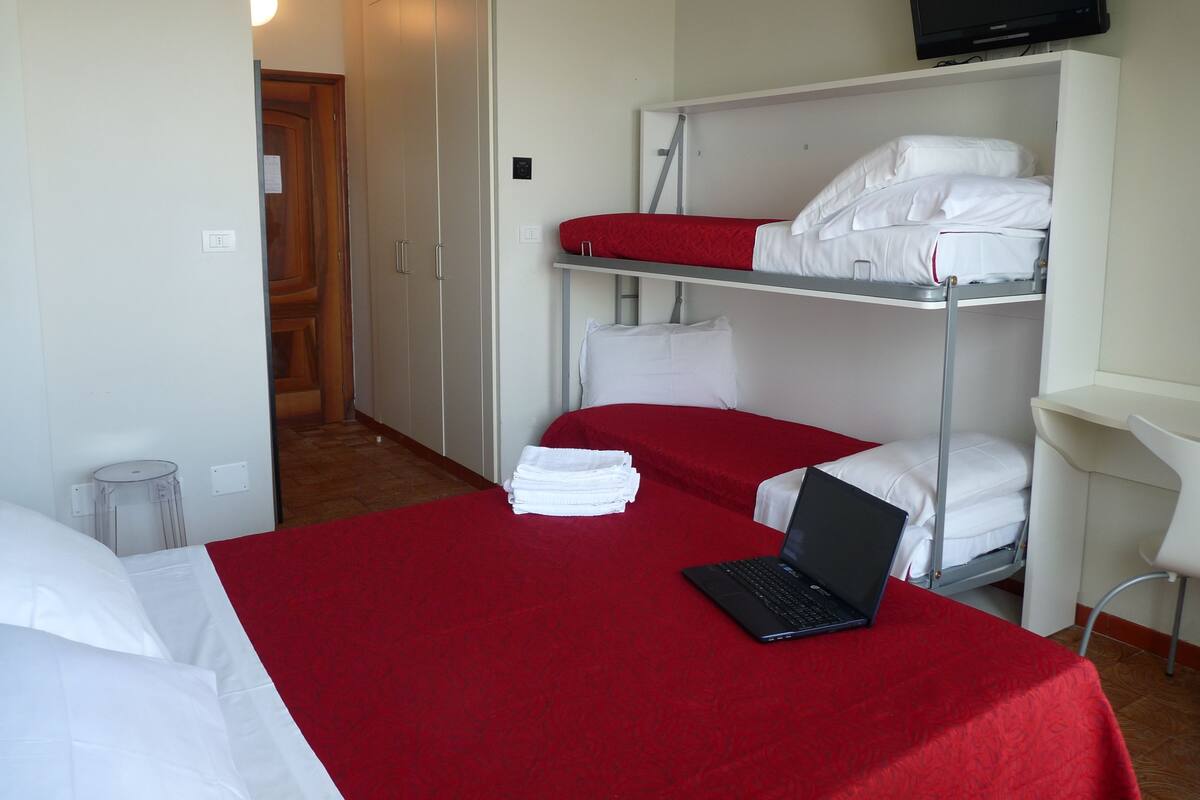 A hotel room with a bunk bed, a desk with a laptop, and a television on the wall.