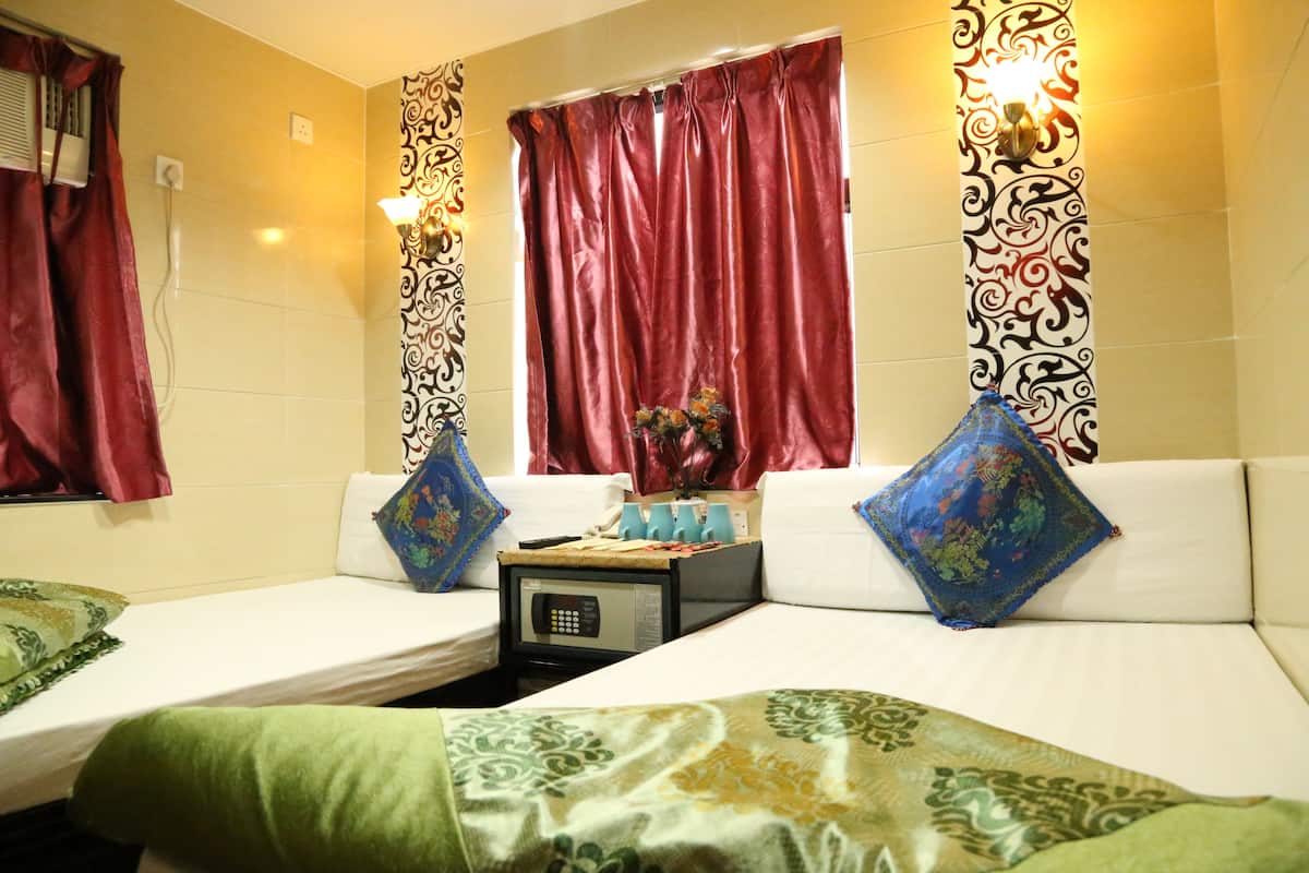 A hotel room with two single beds, a small table with a microwave, and a decorative vase on the windowsill.