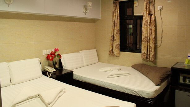 Een hotelkamer met twee bedden, een nachtkastje met een telefoon, een vaas met bloemen en een klok aan de muur.