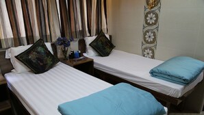 Twee eenpersoonsbedden met blauw-zwarte kussens, een nachtkastje met een afstandsbediening, en een vaas met bloemen.
