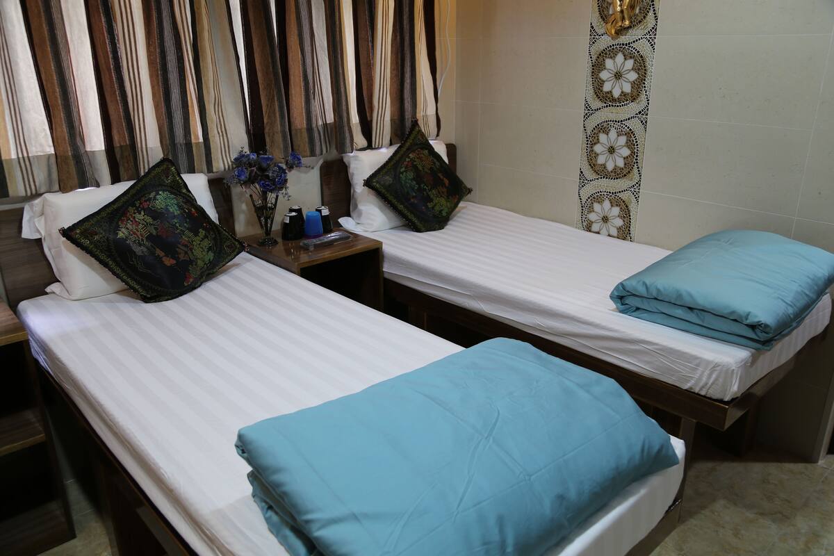 Two single beds with blue and black patterned pillows, a nightstand with a remote control, and a vase with flowers.