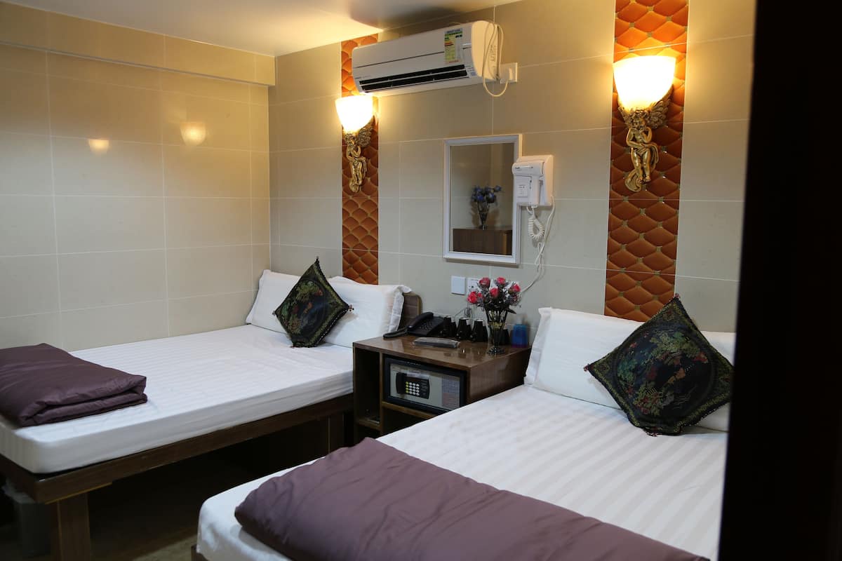 A hotel room with two beds, a bedside table with a phone and a remote control, and an air conditioning unit mounted on the wall.