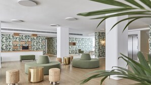 A modern lobby with green seating, wooden flooring, and a tropical wallpaper design.