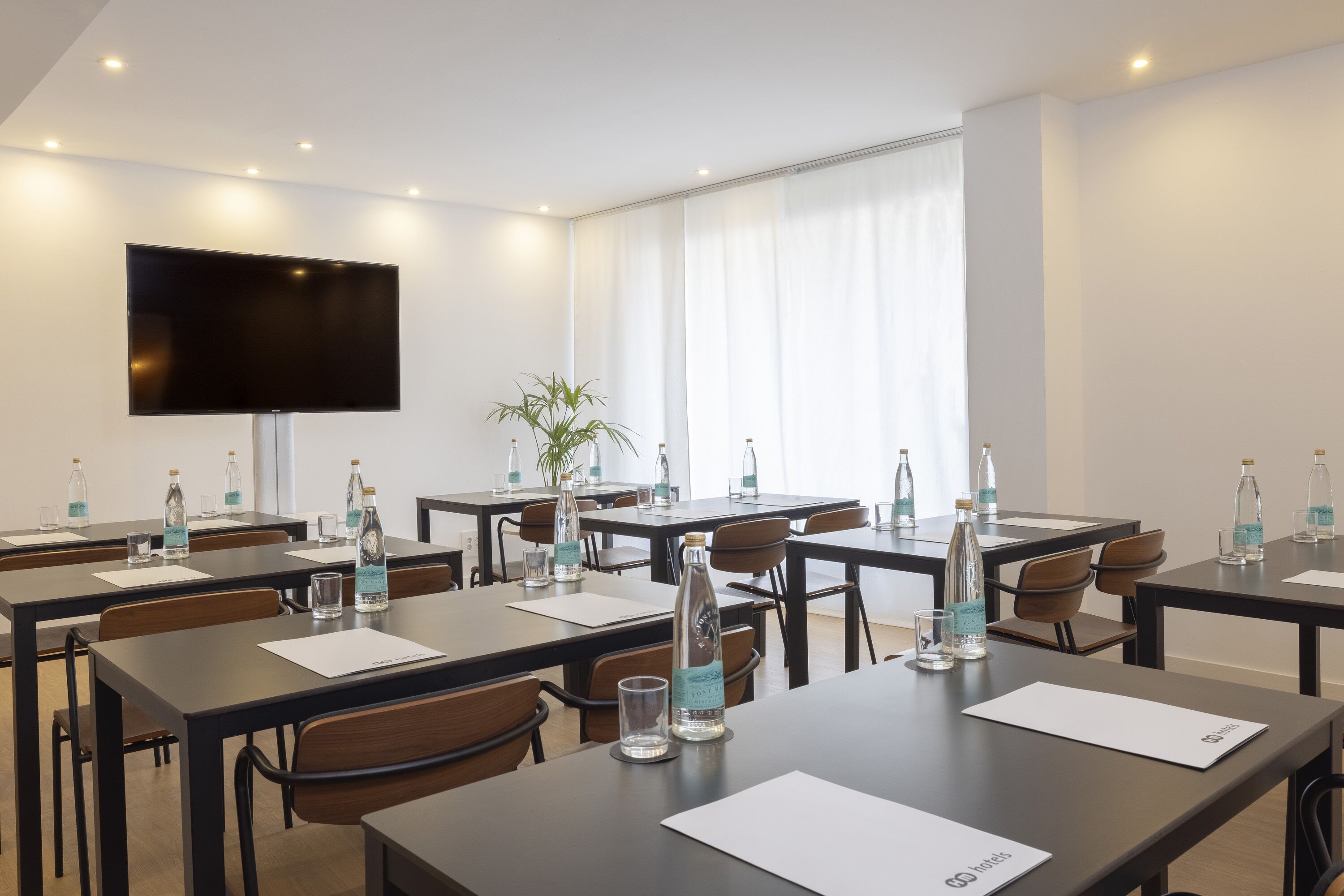 A conference room with tables, chairs, water bottles, and a flat-screen TV.