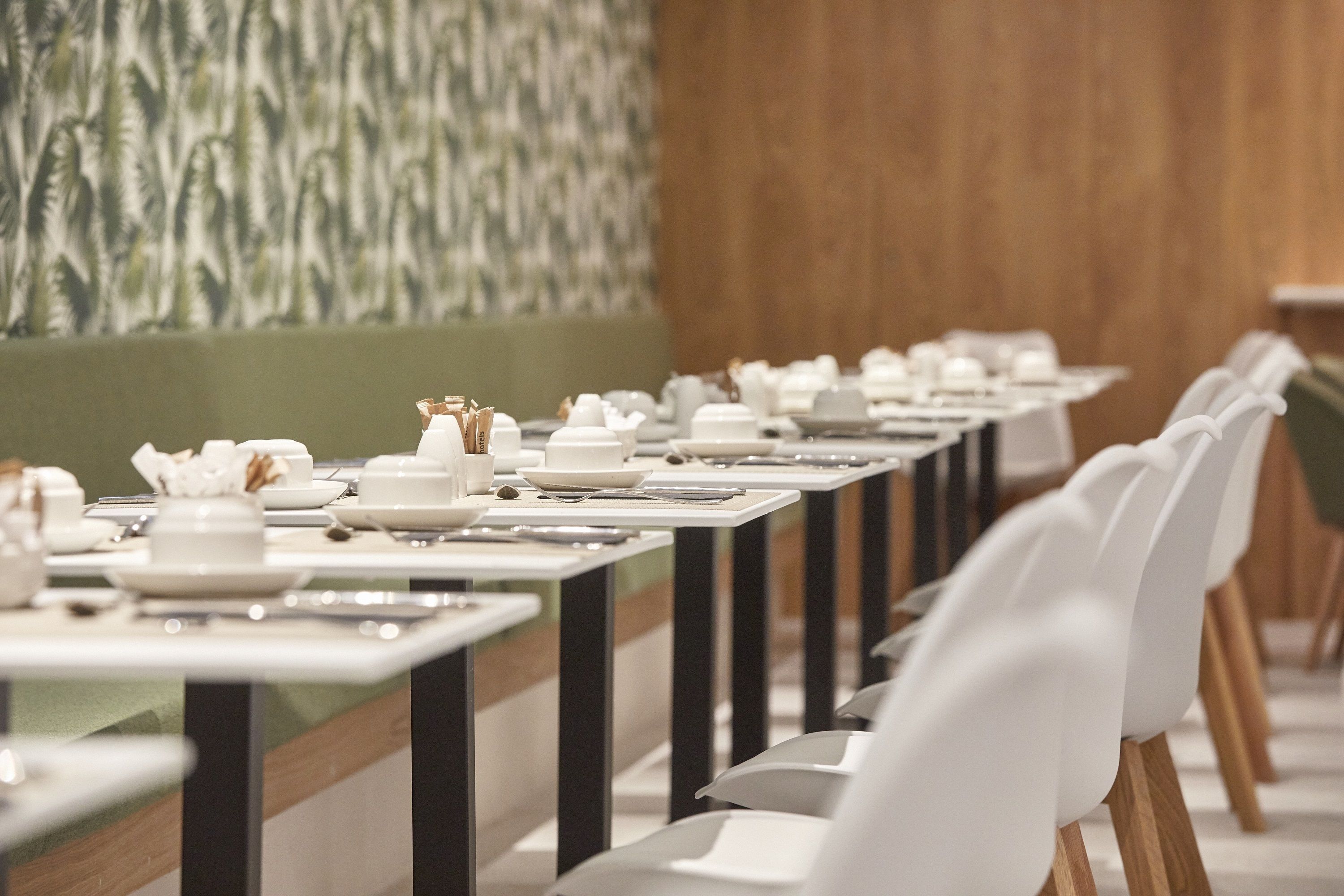 A dining area with tables set for service, chairs aligned, and a patterned wall in the background.
