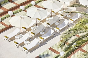 An outdoor seating area with white lounge chairs and tables, arranged in rows with umbrellas providing shade.