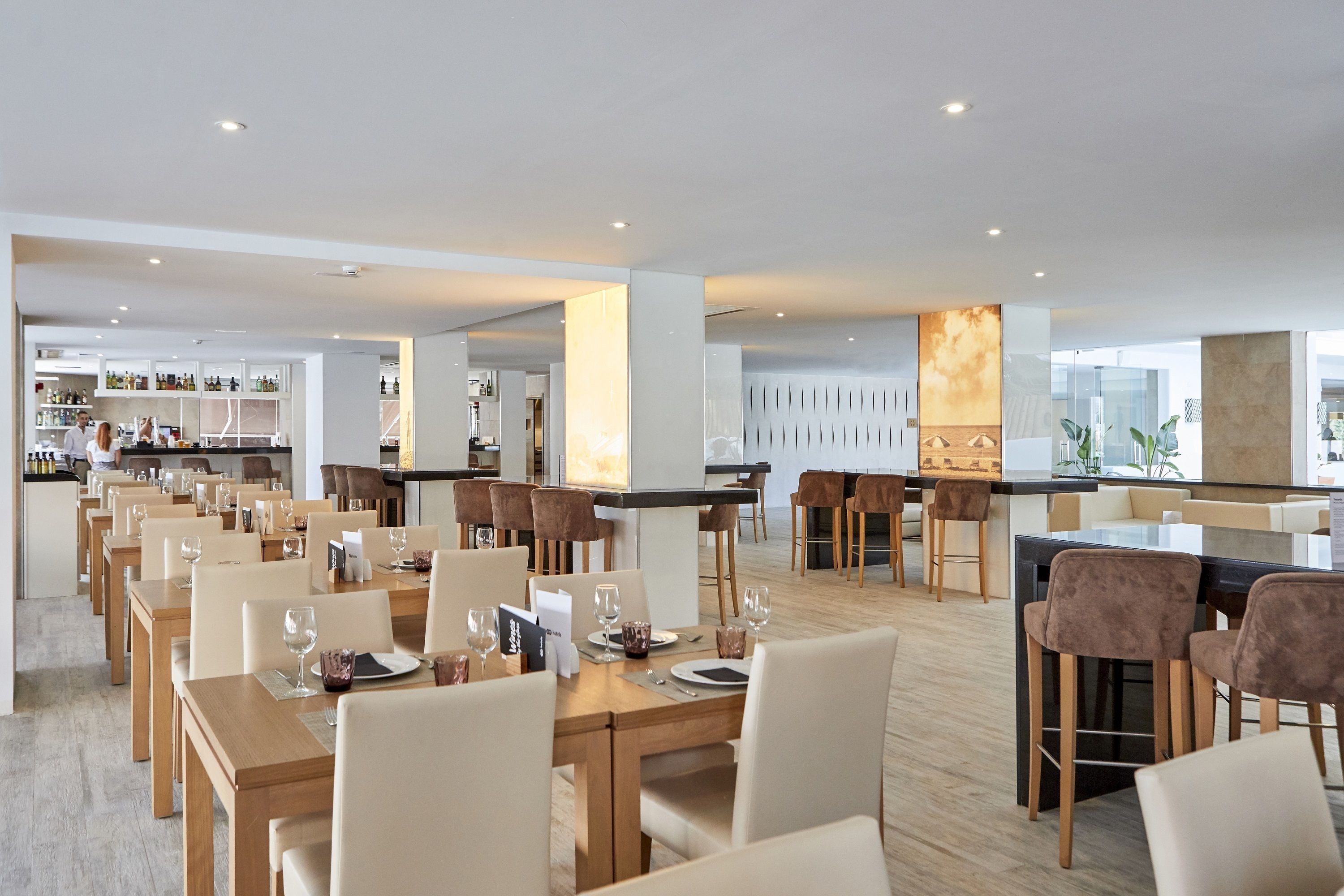 Un espace de restauration moderne avec plusieurs tables et chaises, un bar et une cuisine en arrière-plan.