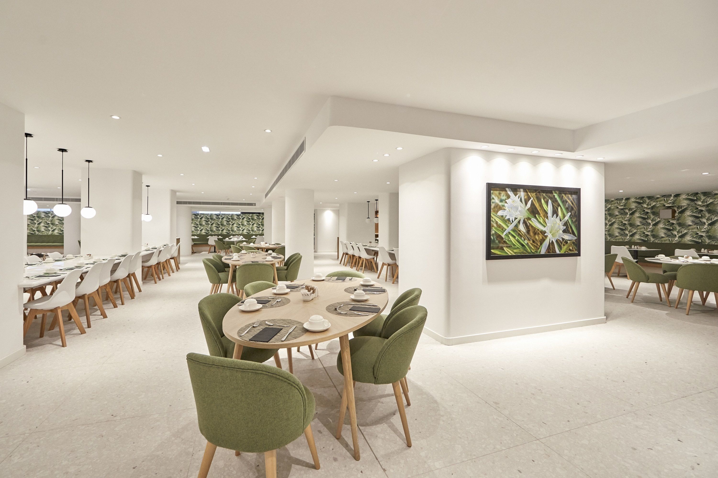 Un comedor moderno con mesas redondas, sillas tapizadas en verde y una gran obra de arte floral enmarcada en la pared.