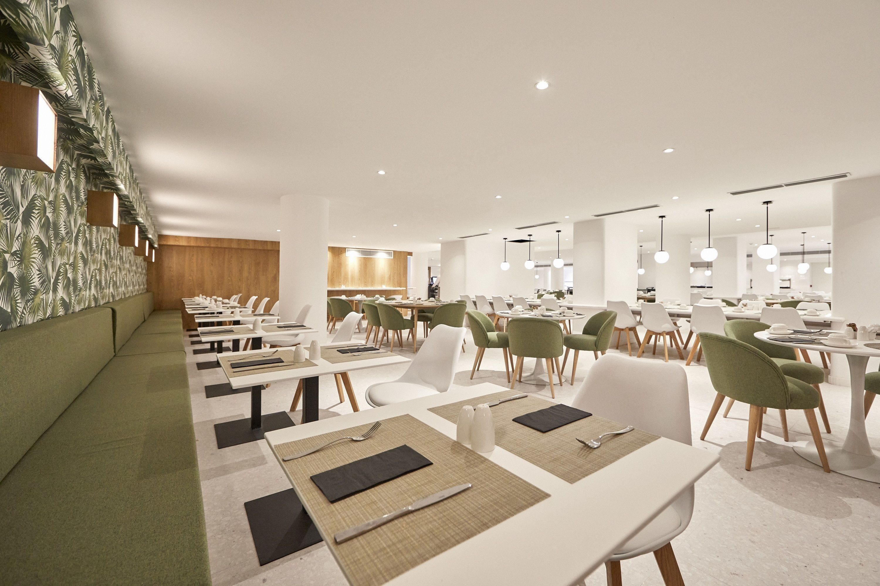 A modern dining area with white tables, green chairs, and a patterned wall.