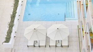 A rooftop pool area with white umbrellas and lounge chairs.
