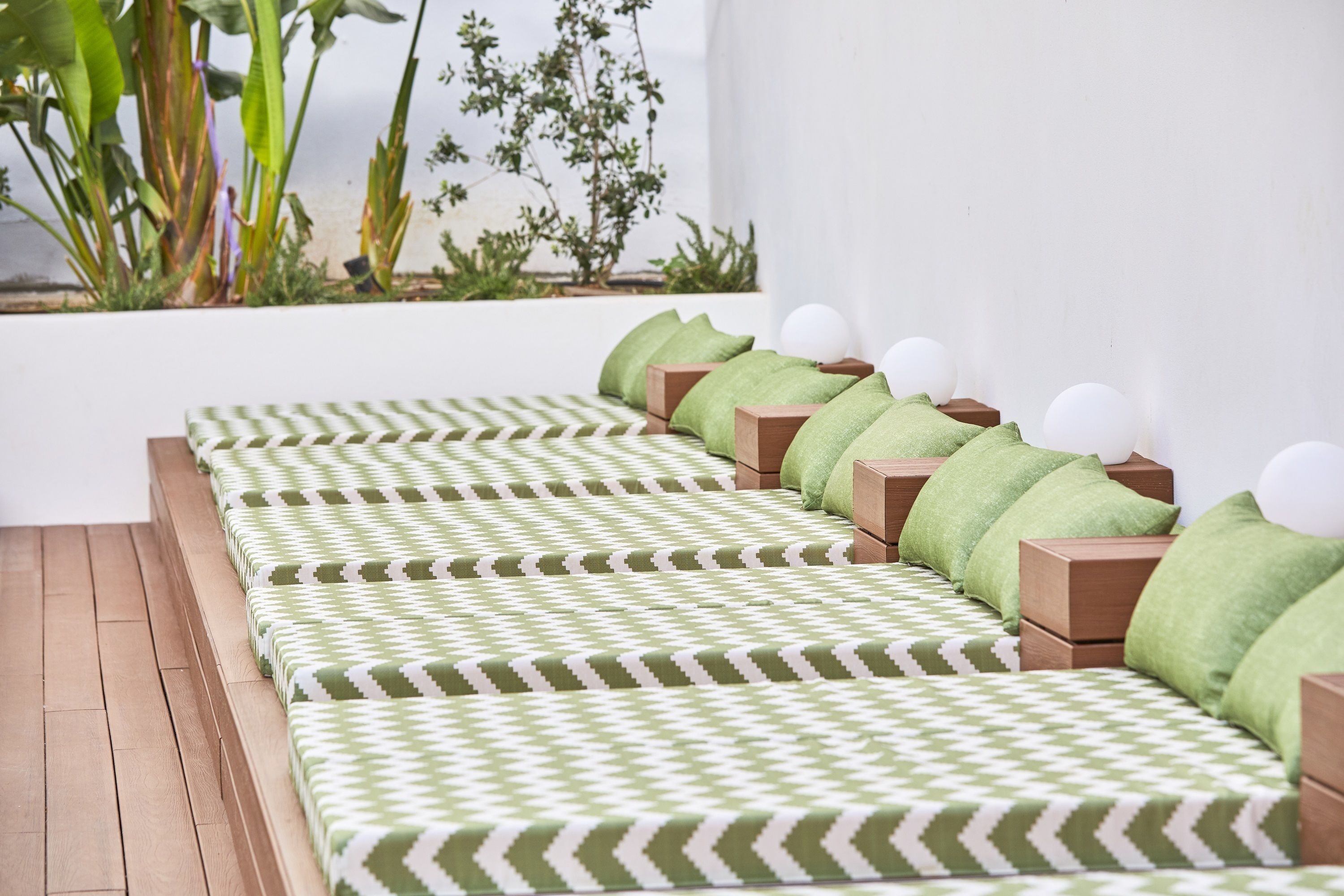 A row of wooden beds with green and white checkered bedding, each with a green pillow and a white spherical object on the headboard.