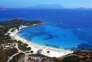 An aerial view of a coastal area with a beach, boats, and parked cars.