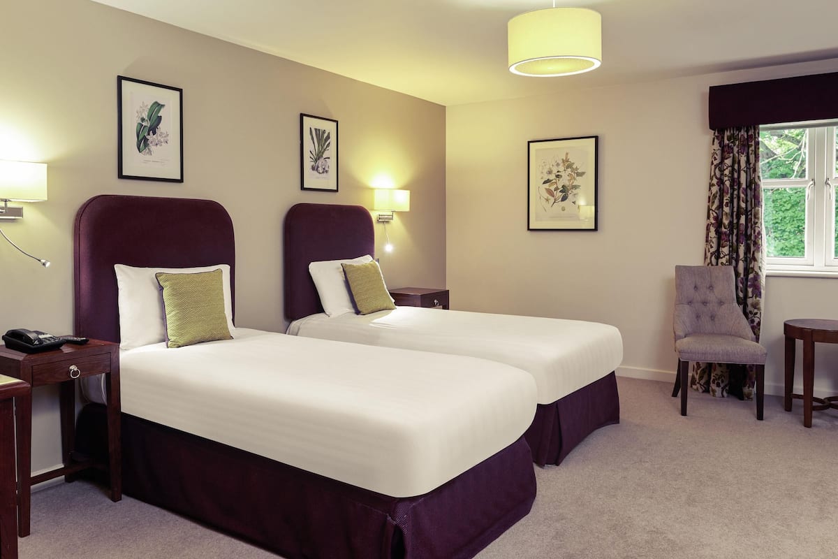A hotel room with two beds, a chair, a desk, and framed botanical prints on the wall.