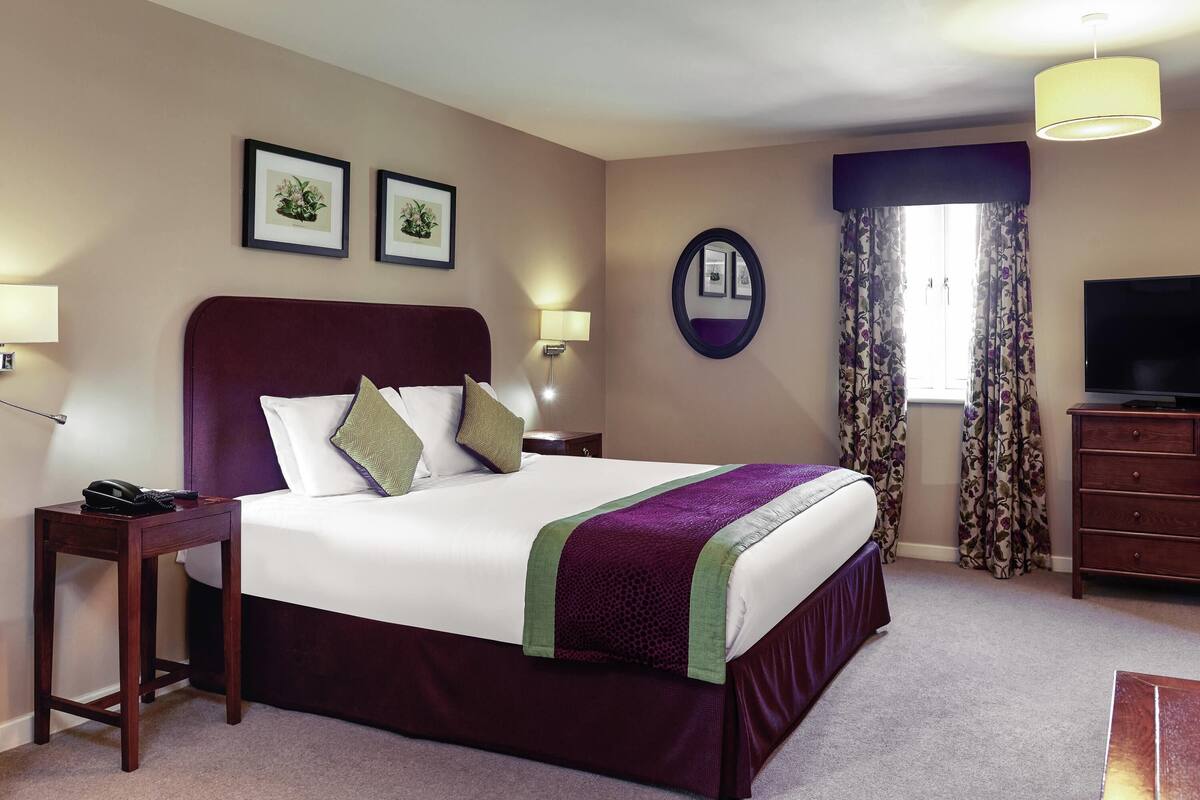 A hotel room with a large bed, a TV, a desk with a phone, and framed pictures on the wall.