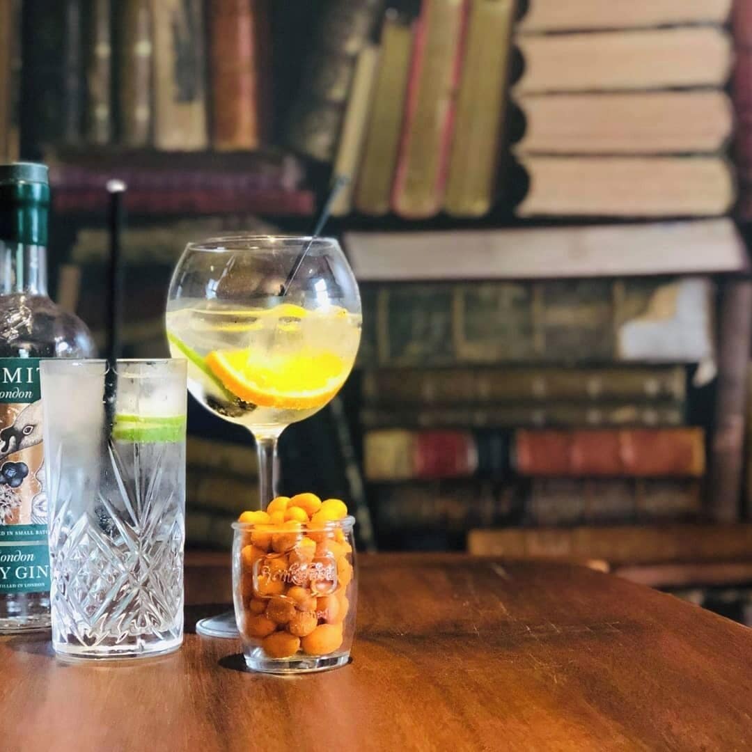 A table with two glasses of gin, one with a lemon slice, and a jar of nuts.