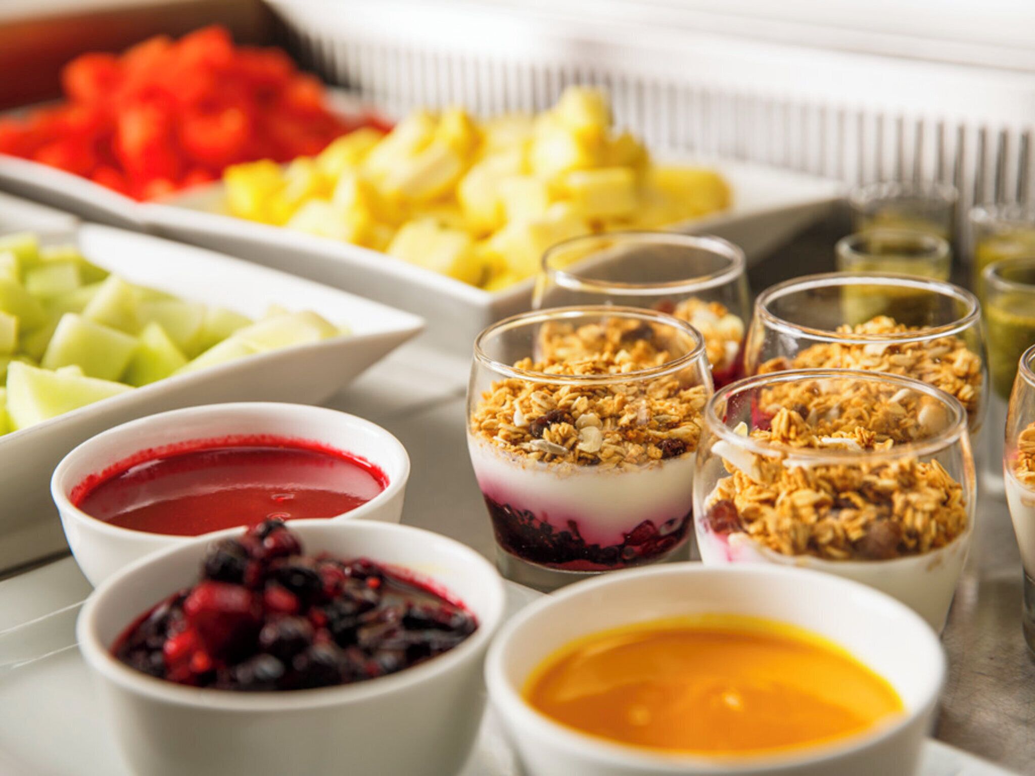 Una selezione di cibi, tra cui frutta, granola e dolci, in ciotole e bicchieri.