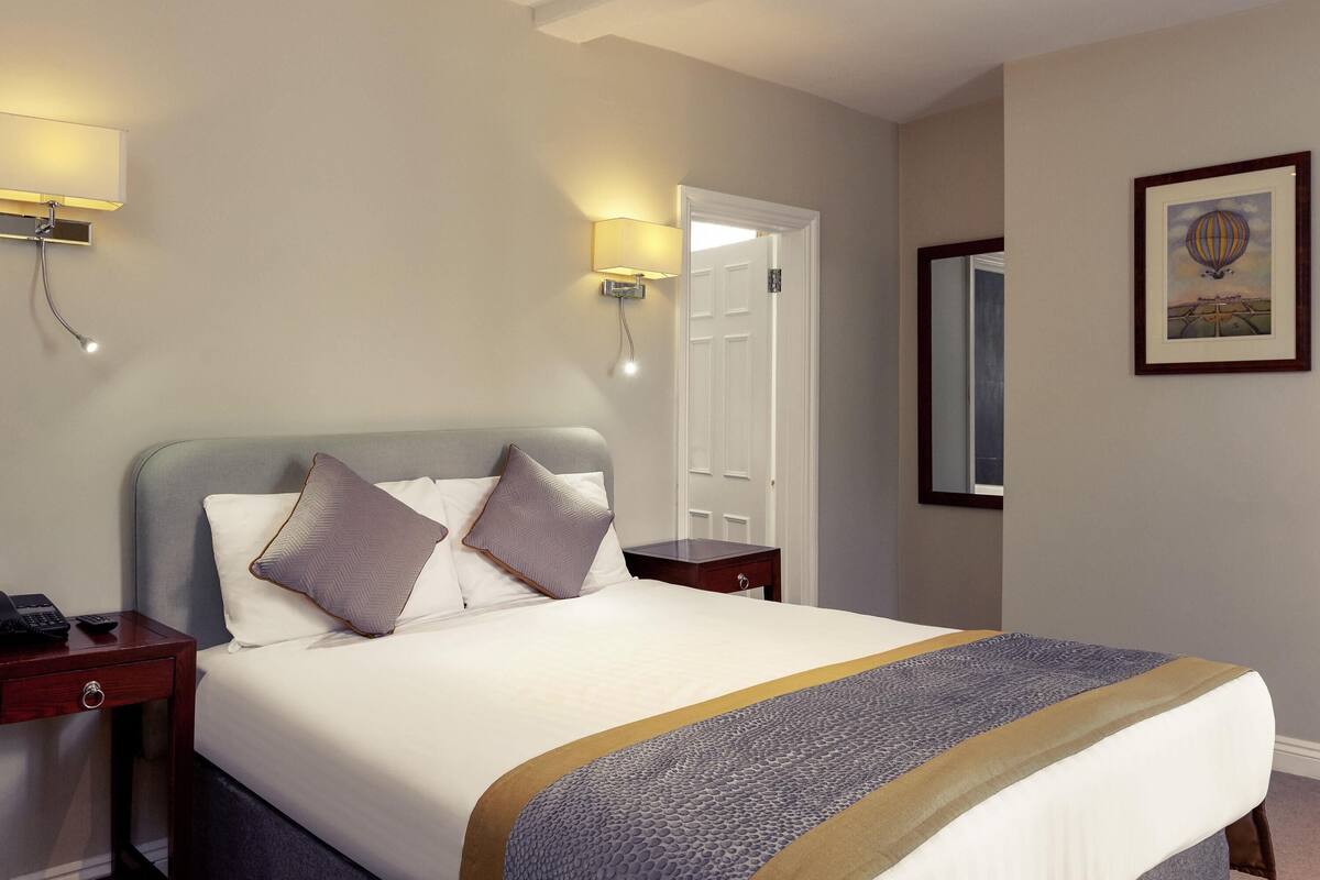 A hotel room with a bed, bedside tables, a lamp, a door, and a framed picture on the wall.