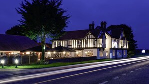 A large, traditional building with multiple windows and a prominent chimney, situated beside a road with light trails indicating traffic. - Mercure Thame Lambert Hotel (Watlington)