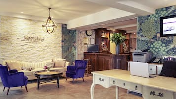 Un vestíbulo de hotel con una pared de piedra, una zona de bar, un sofá, una mesa de centro y un escritorio con una computadora.
