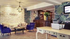Un'accogliente hall d'hotel con parete in pietra, angolo bar, divano, tavolino da caffè e scrivania con computer.