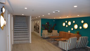 Ein modernes Interieur mit einer Treppe, gestreiften Sesseln, einem Holztisch und einer Türkiswand mit runden Leuchten.